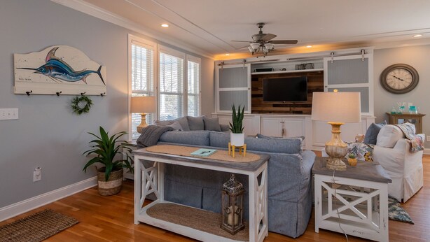 A living room with a sofa, a coffee table, a TV, and a ceiling fan. - The Sassy Seahorse: Spacious Beach Home with Multiple Living Areas and Room for (Oak Island)
