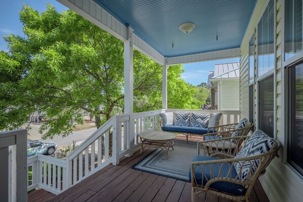 A covered porch with a white railing, wicker furniture, and a view of the street.