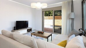 Ein modernes Wohnzimmer mit Sofa, Couchtisch, Flachbildfernseher und einer Glastür, die zu einem Außenbereich führt.