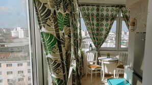 Un balcó amb vista a edificis, una taula petita amb cadires i cortines amb dibuixos de fulles.
