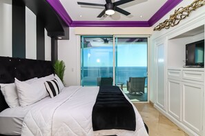 Habitación de hotel con cama, ventilador de techo, televisión y balcón con vistas.