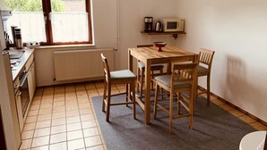 Ett litet kök med ett matbord, stolar, en mikrovågsugn och ett fönster med utsikt över träd.