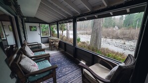 A cozy room with wooden furniture, a large window, and a view of a natural landscape. - Riverside Mid-Century Cabin with Mountain Views (Baring)
