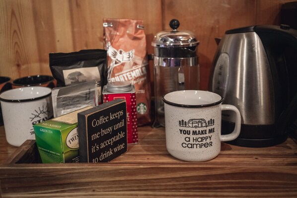 Una encimera de cocina con cafetera, hervidor, taza, caja de té verde, bolsa de café y un cartel.