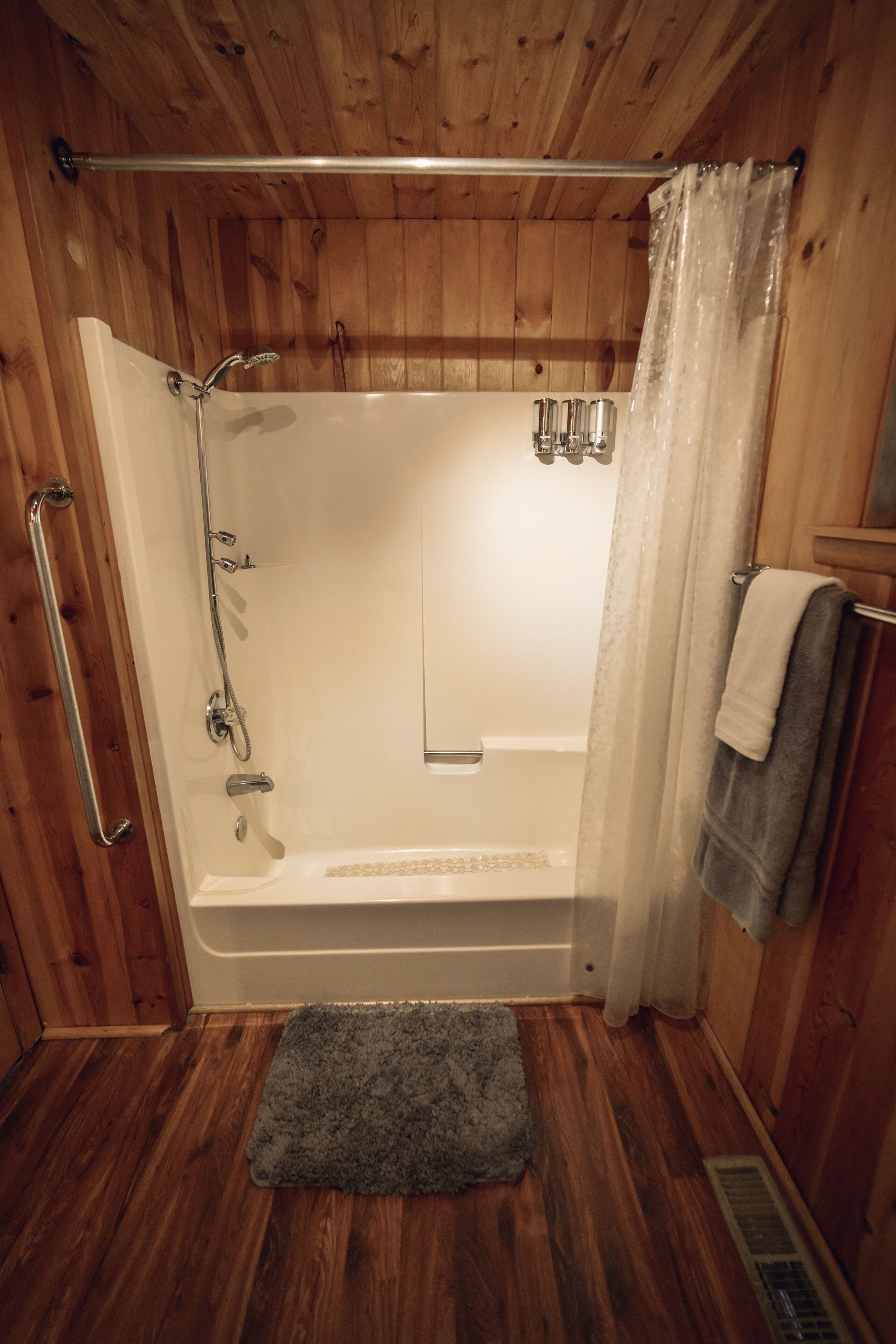 A wooden-paneled bathroom with a bathtub, shower, and grab bars.