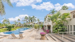 Un área de piscina en un resort, con múltiples sillas de descanso, una piscina y palmeras.