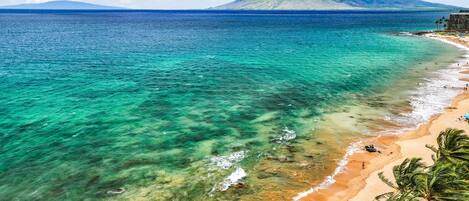 Una playa con agua turquesa cristalina, una orilla arenosa y una montaña al fondo.