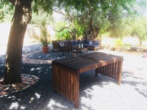 Un espace extérieur aménagé avec une table et des chaises en bois, entouré d’arbres et de plantes en pot.