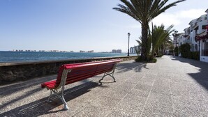 A bench by the seaside with a clear view of the ocean and buildings in the distance. - Duplex Aldeas Taray Club 55 Admer (La Manga del Mar Menor)