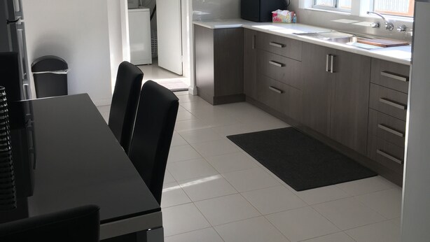 A modern kitchen with grey cabinets, a black dining table, and a black rug. - Entire House 3 bedrooms, 5 minute walk to town centre and 1 minute to beach (Strahan)