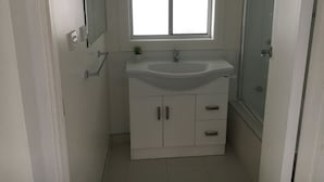 A bathroom with a white sink, a mirror, a small potted plant, and a glass shower enclosure. - Entire House 3 bedrooms, 5 minute walk to town centre and 1 minute to beach (Strahan)