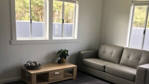 A living room with a grey carpet, a beige sofa, a wooden coffee table, and two windows with blinds. - Entire House 3 bedrooms, 5 minute walk to town centre and 1 minute to beach (Strahan)
