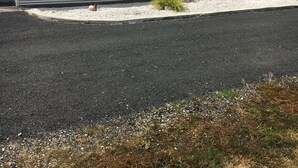 A single-story building with a corrugated metal roof, large windows, and a gravel driveway. - Entire House 3 bedrooms, 5 minute walk to town centre and 1 minute to beach (Strahan)
