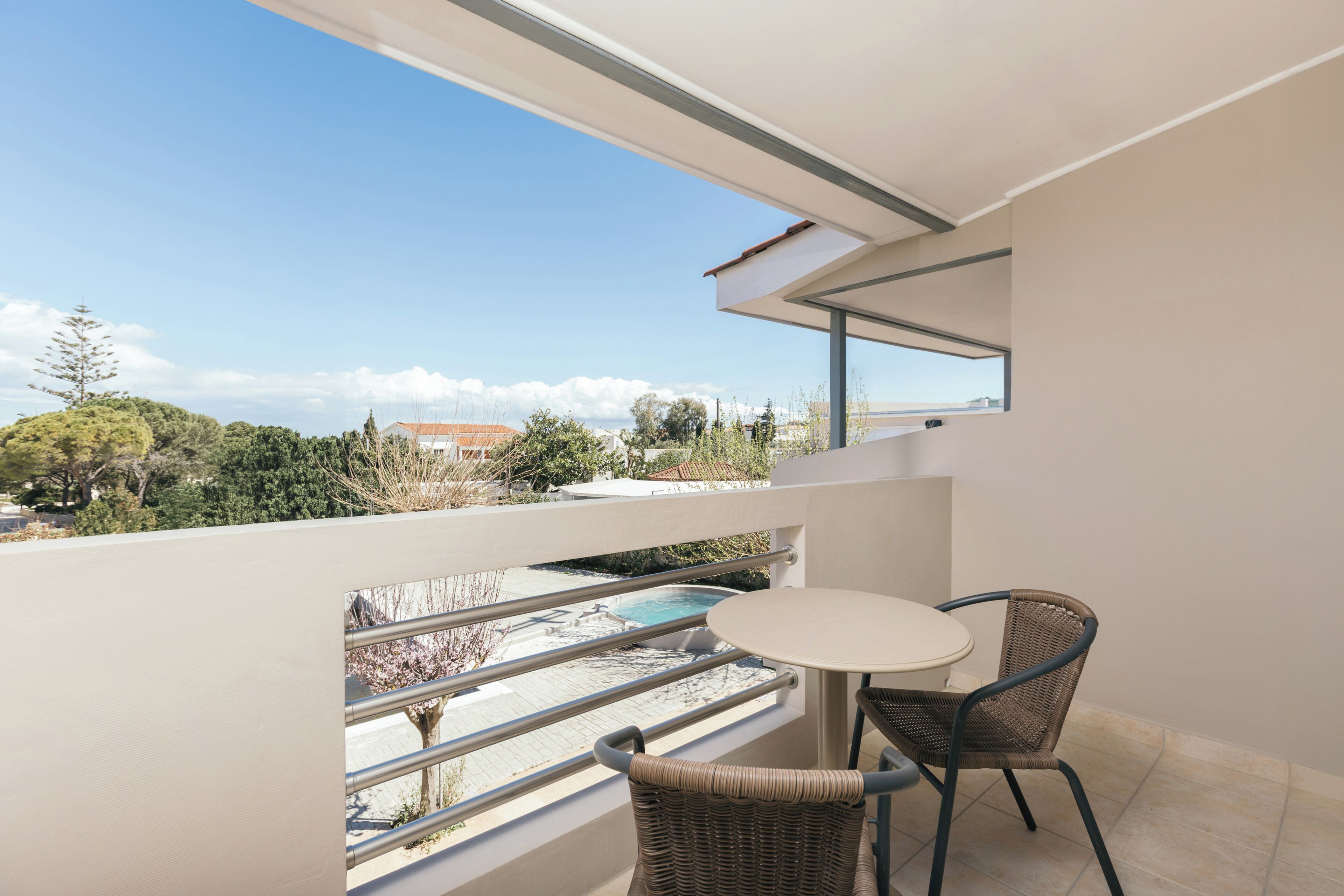 A balcony with a table and chairs, overlooking a pool and greenery.