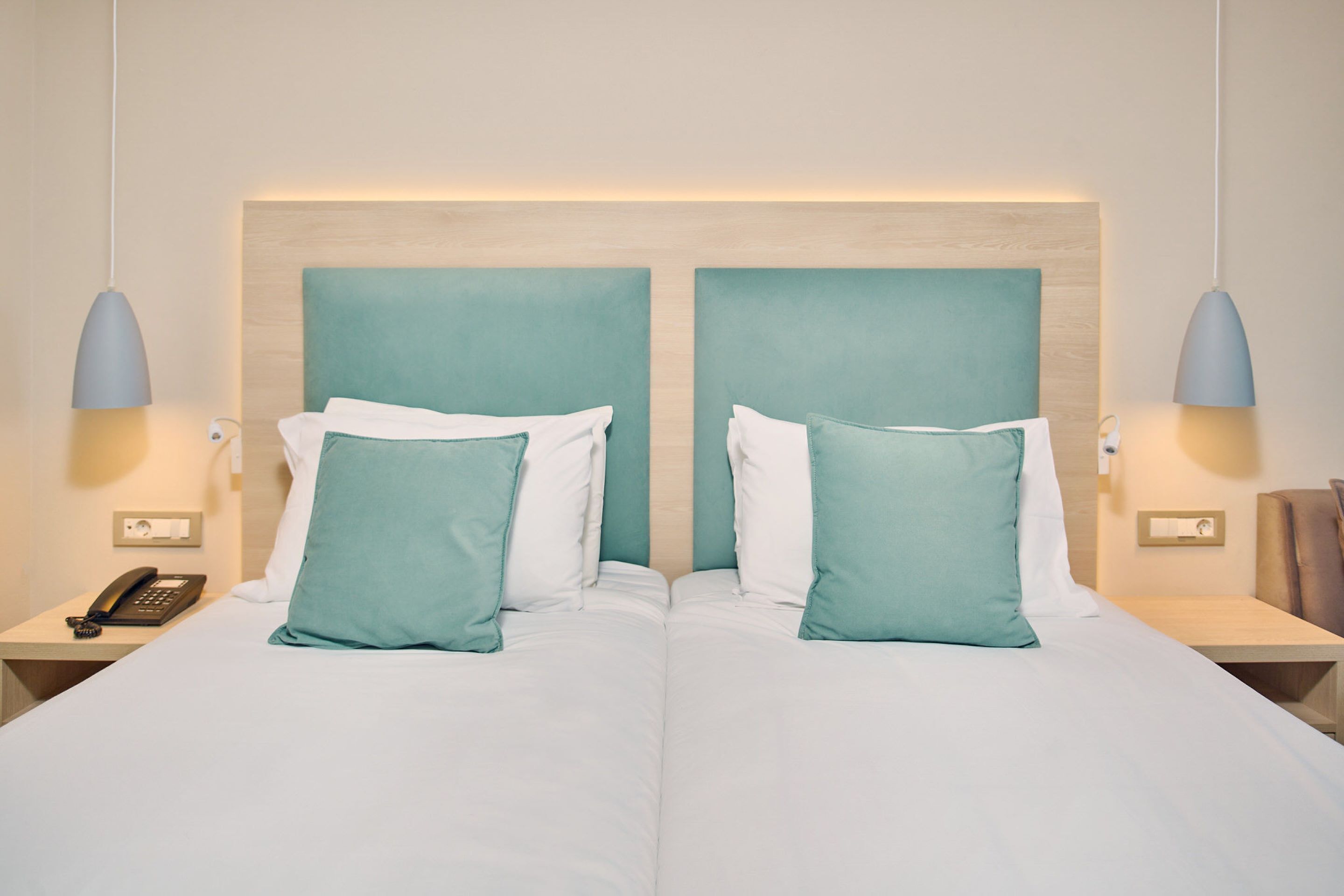 Un lit double avec une literie aux couleurs turquoise et blanche, deux lampes de chevet et un téléphone sur la table de chevet.