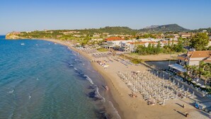 A coastal beach with clear waters, a sandy shore, and a row of beach umbrellas and sun loungers. - Tsilivi Beach Hotel (Zakynthos)