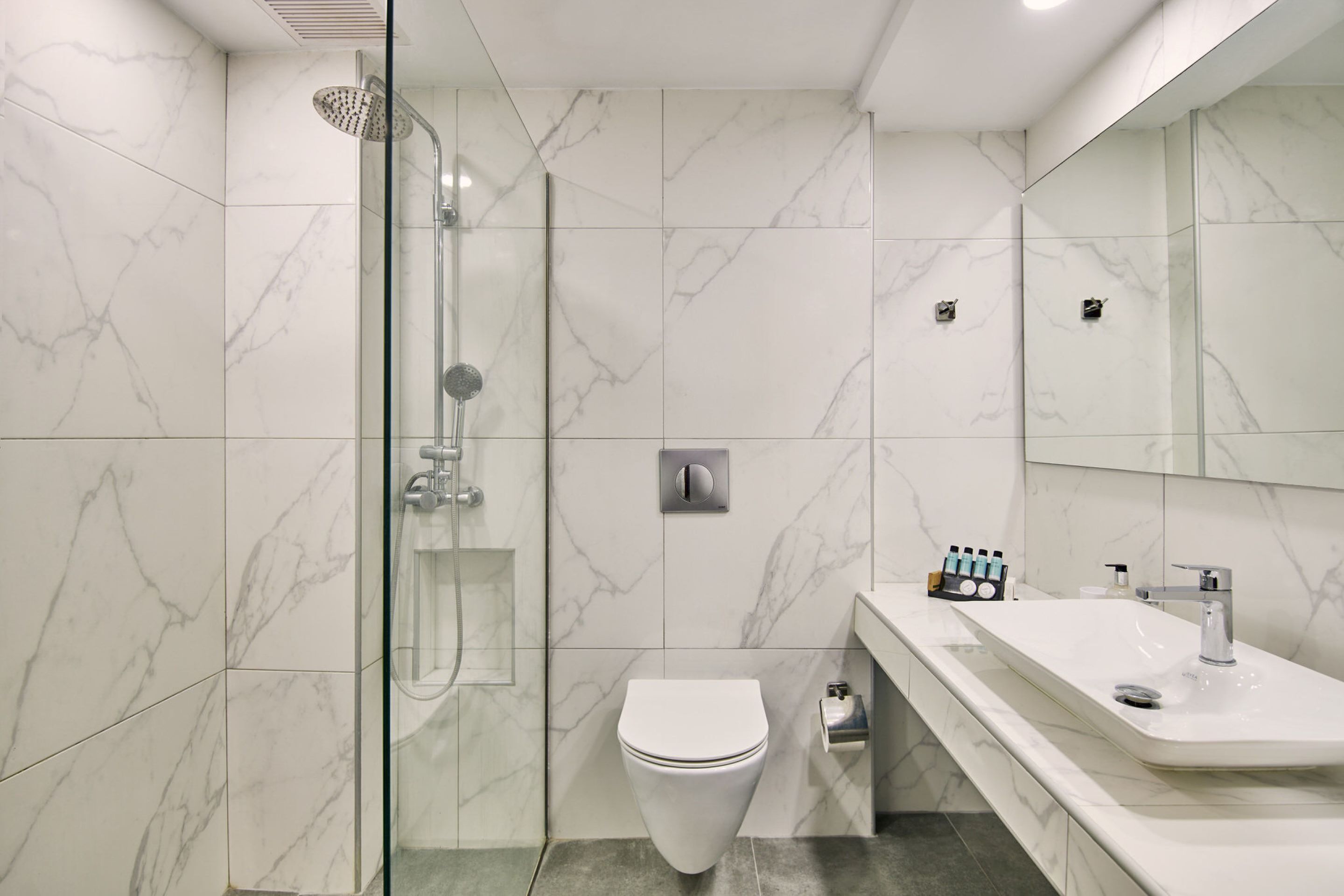 Un baño moderno con cabina de ducha de vidrio, inodoro blanco y tocador con lavamanos y espejo.