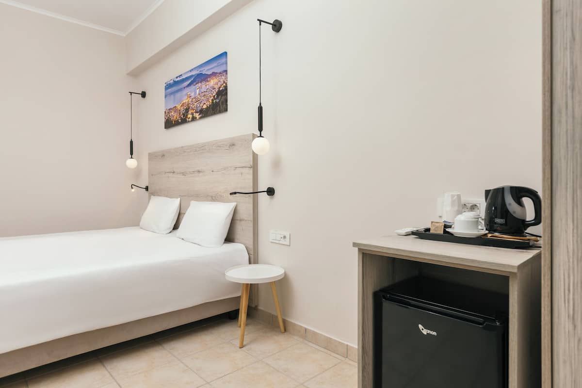 Quarto de hotel moderno com uma cama, uma pequena mesa redonda, uma máquina de café e um frigorífico.