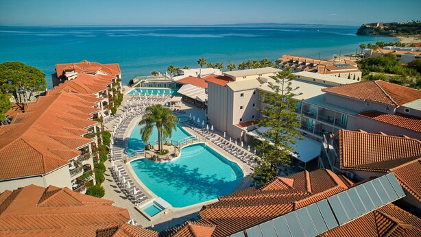 A resort with a large swimming pool surrounded by lounge chairs, a separate pool, and a view of the sea. - Tsilivi Beach Hotel (Zakynthos)