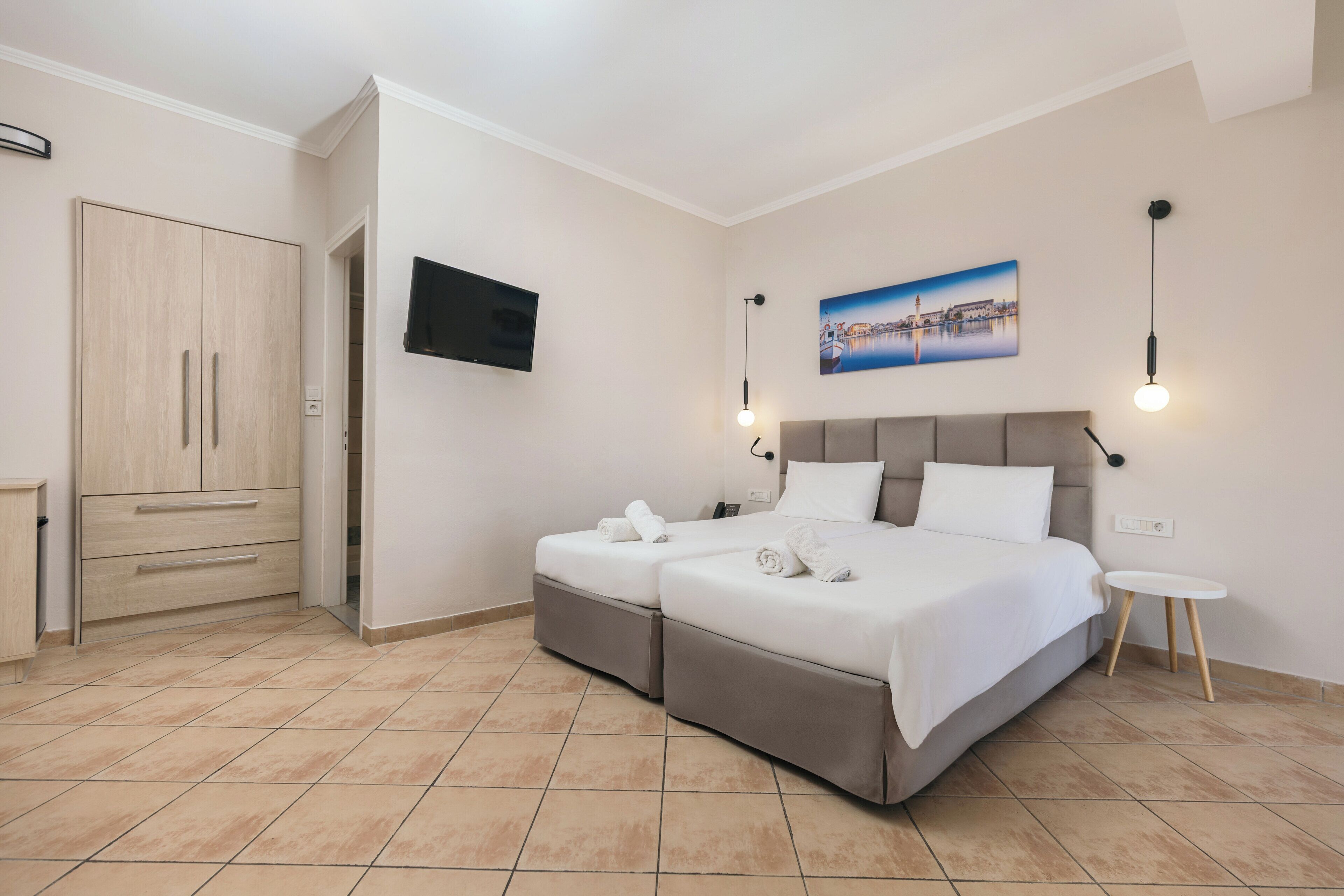 A bedroom with two beds, a TV, a painting, and a small table.