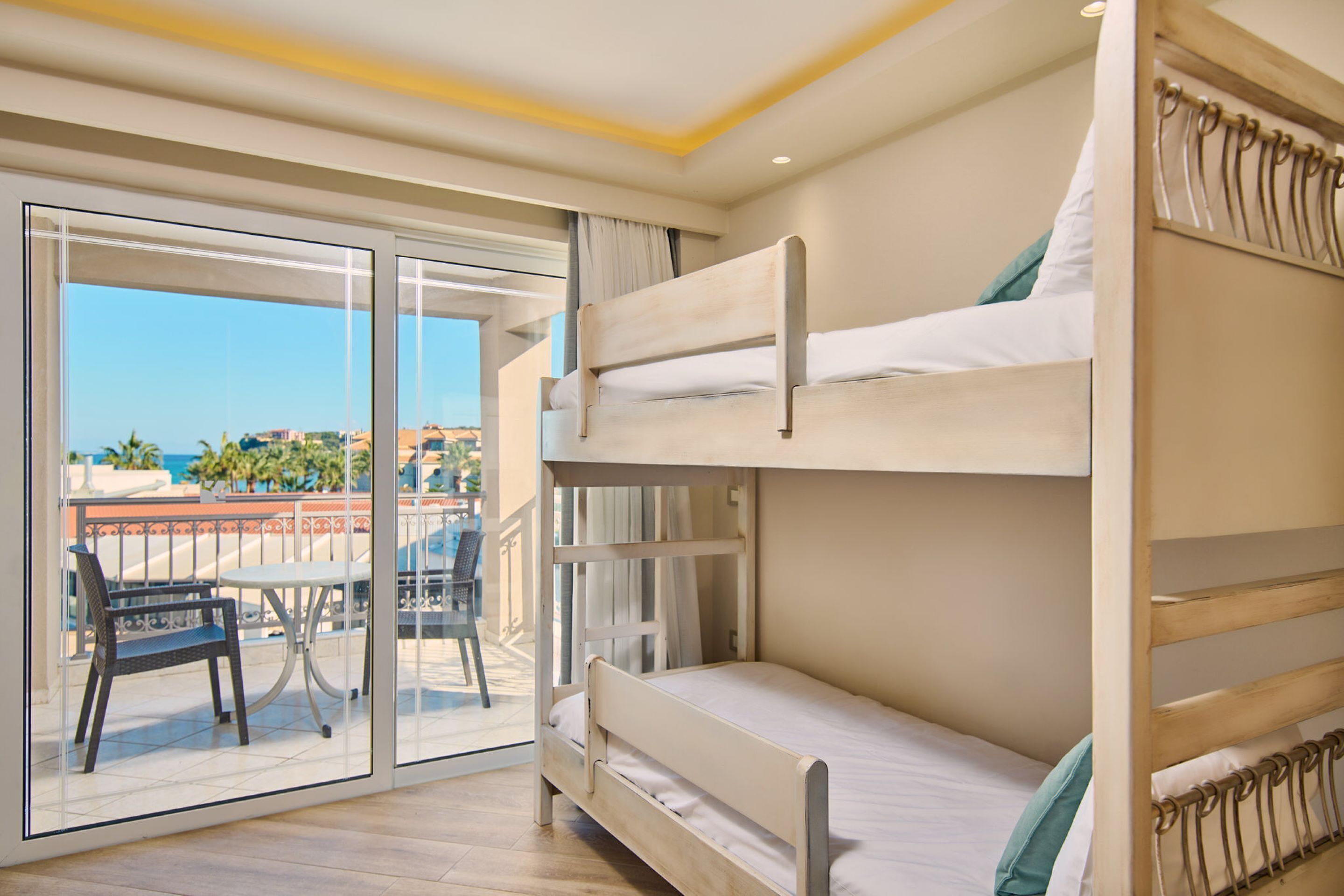 A room with bunk beds, a balcony with a table and chairs, and a view of the city.