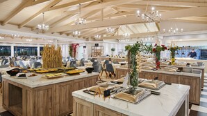 A spacious buffet area with multiple serving stations, wooden paneling, and modern chandeliers. - Tsilivi Beach Hotel (Zakynthos)