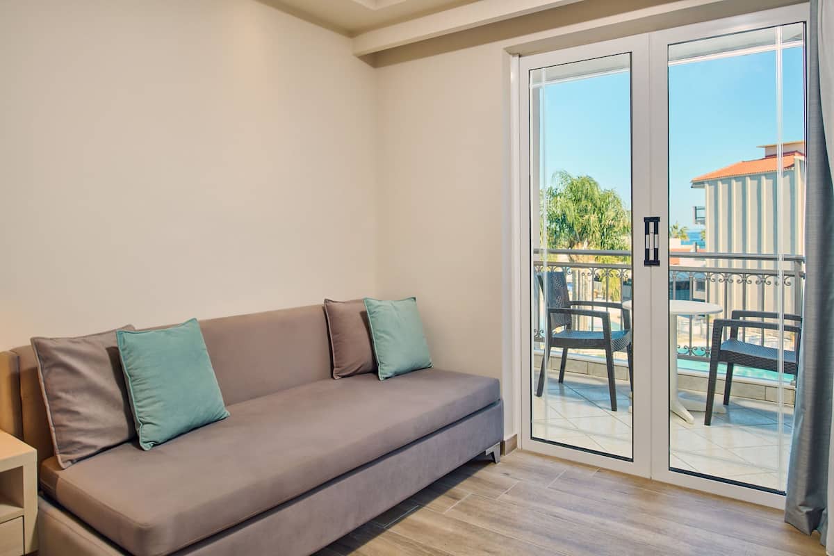 Uma sala de estar moderna com um sofá, duas almofadas e uma porta de vidro deslizante que dá para uma área externa com cadeiras e uma mesa.