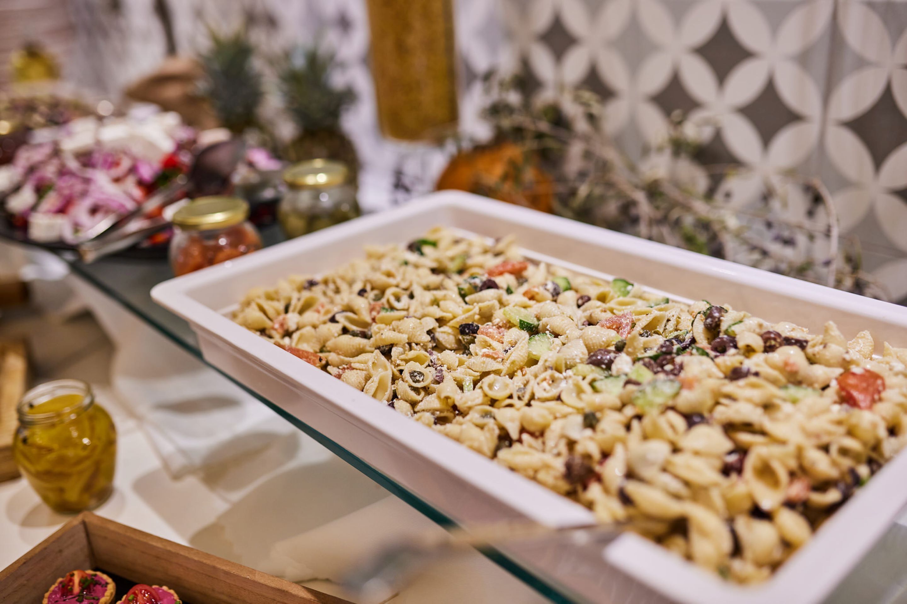 Una mesa de bufé con ensalada de pasta, diferentes condimentos y elementos decorativos.