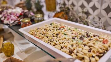 Una mesa de bufé con ensalada de pasta, diferentes condimentos y elementos decorativos.