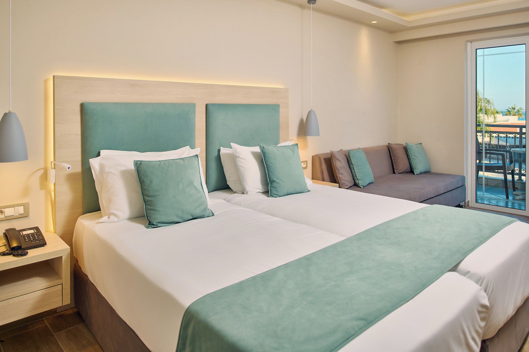 A hotel room with two beds, a sofa, a nightstand with a phone, and a balcony with a view.