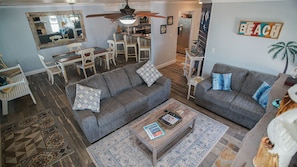 A spacious living room with two grey sofas, a coffee table, and a dining area with a kitchen in the background.