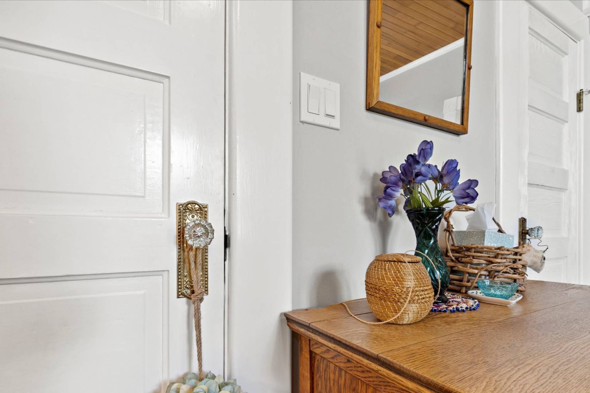 A wooden dresser with a vase of purple flowers, a woven basket, and a small blue glass bowl.