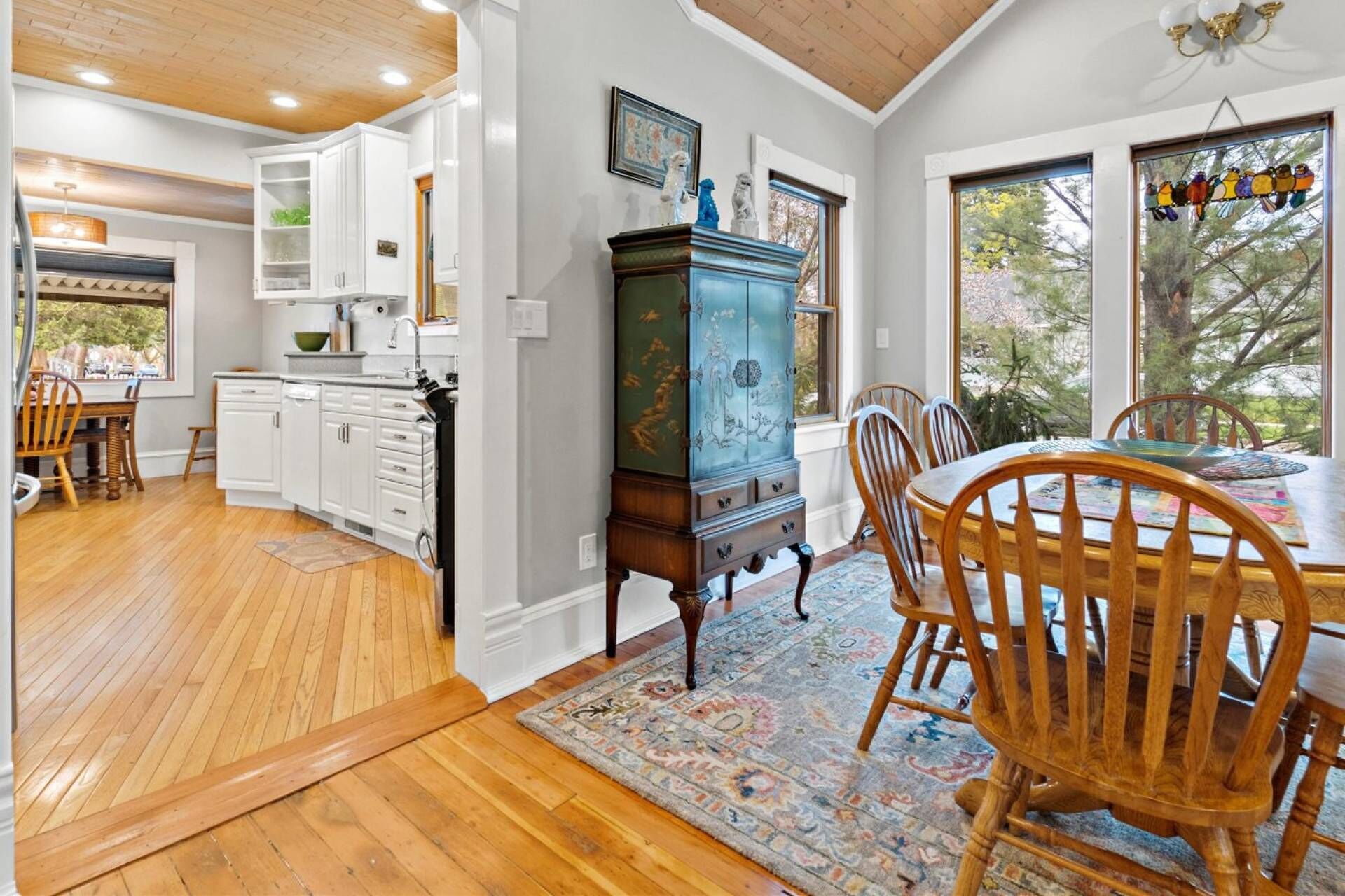 A kitchen with white cabinets, a wooden dining table with chairs, and a patterned rug.