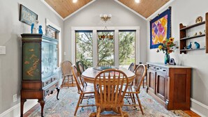 A dining area with a round table, wooden chairs, a patterned rug, and a view through large windows. - Cozy North End Cottage! Walk the Tree-lined Neighborhood to Hyde Park + Camel's Back Park (Boise)