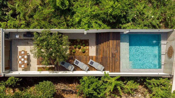 Vista aérea de una villa moderna con piscina, mobiliario exterior y exuberante vegetación.