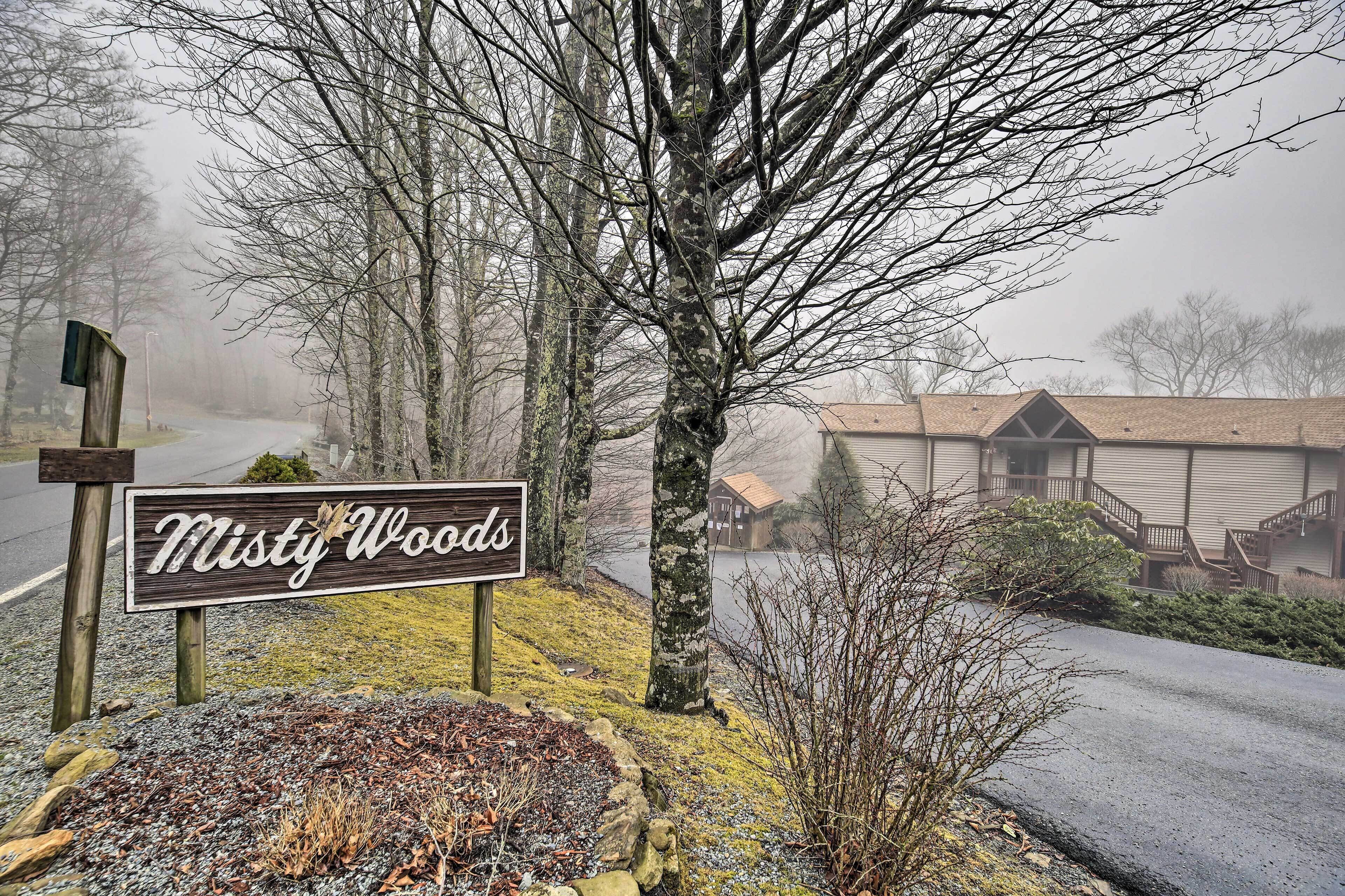 A sign for 'Misty Woods' with a gravel path and trees in the background.