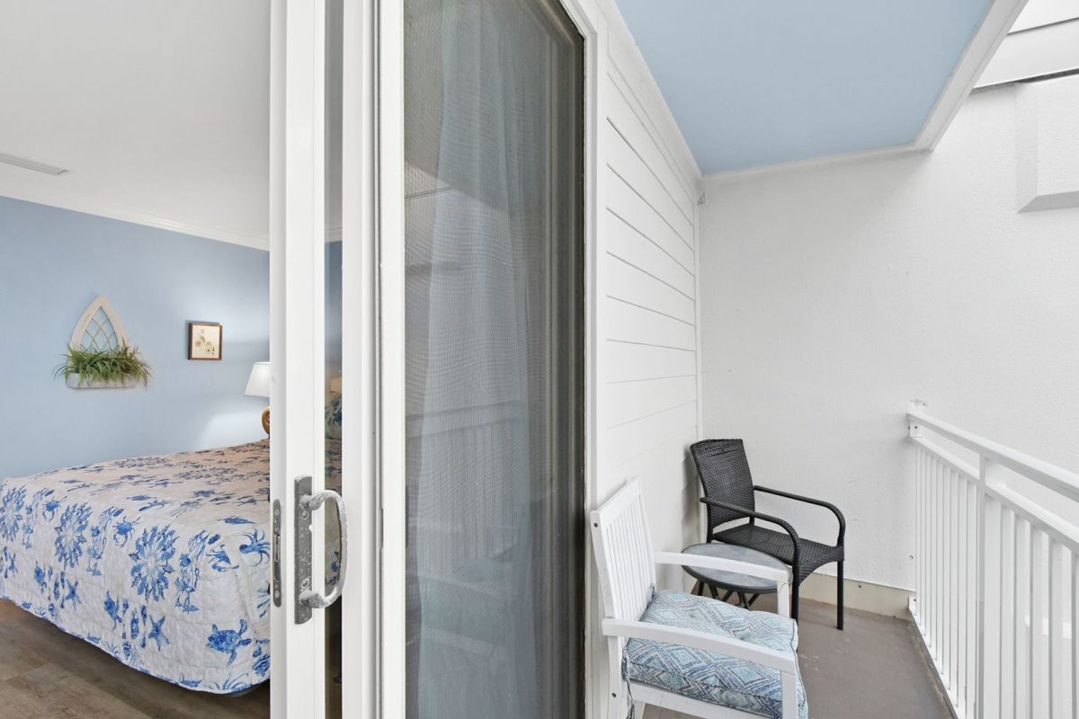 A room with a bed, a chair, and a balcony with a railing.