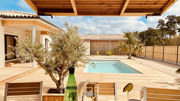 A wooden deck with a pool, outdoor seating, and a view of a house with a tiled roof.