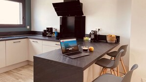 A modern kitchen with a laptop on the island, a coffee maker, and a basket of bread.