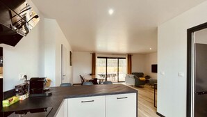 A modern kitchen with a central island, a dining area with a table and chairs, and a living space with a sofa and a TV.