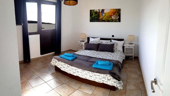 A bedroom with a bed, two bedside tables, a window, and a painting on the wall.