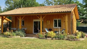 Una cabaña de madera con techo de tejas, un porche con asientos y un jardín delantero.