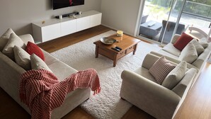Een moderne woonkamer met een grote flatscreen-tv, een witte salontafel en een gezellige zithoek met twee banken en een bijzettafeltje.