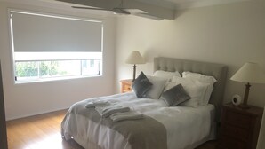 Een slaapkamer met een groot bed, twee nachtkastjes met lampen, een plafondventilator en een raam met uitzicht op groen.