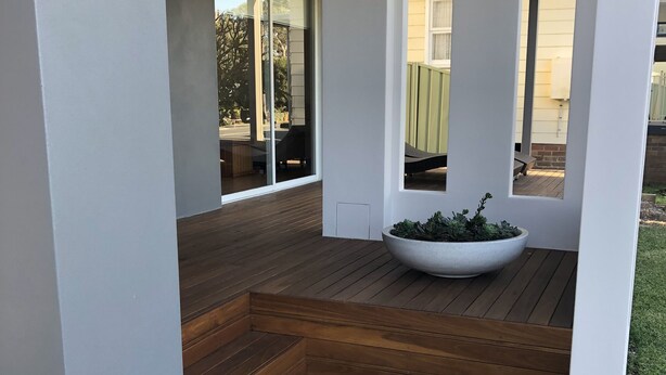 Een moderne patio met een houten terras, een grote plantenbak en uitzicht op de achtertuin.