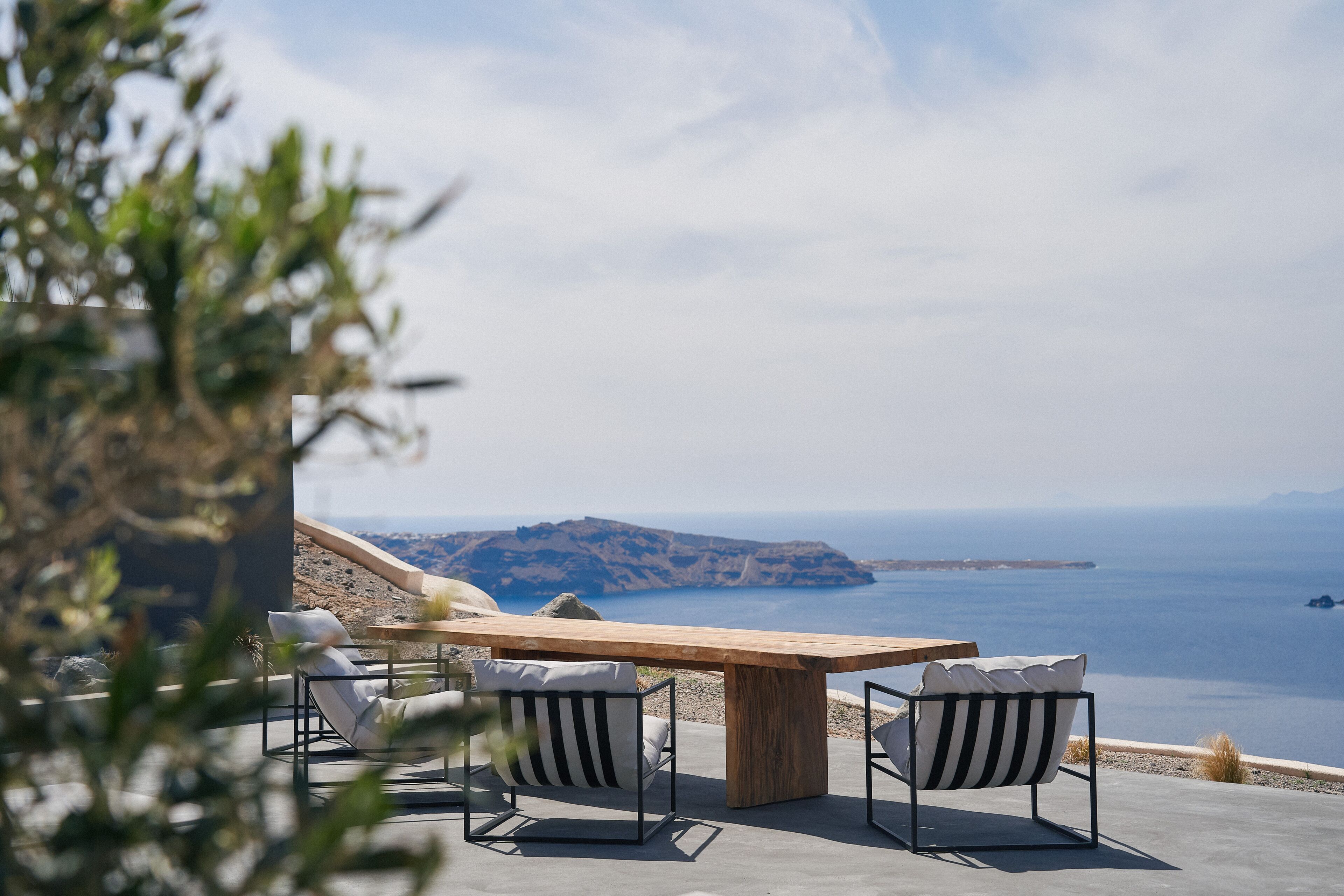 A wooden table with two chairs, a view of the sea, and rocky terrain in the background.