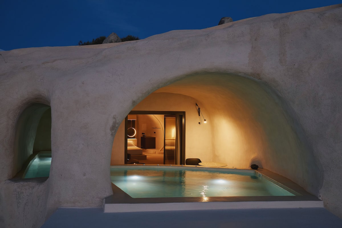 An underground swimming pool with a warm light source, a doorway leading to a room, and a stone exterior.