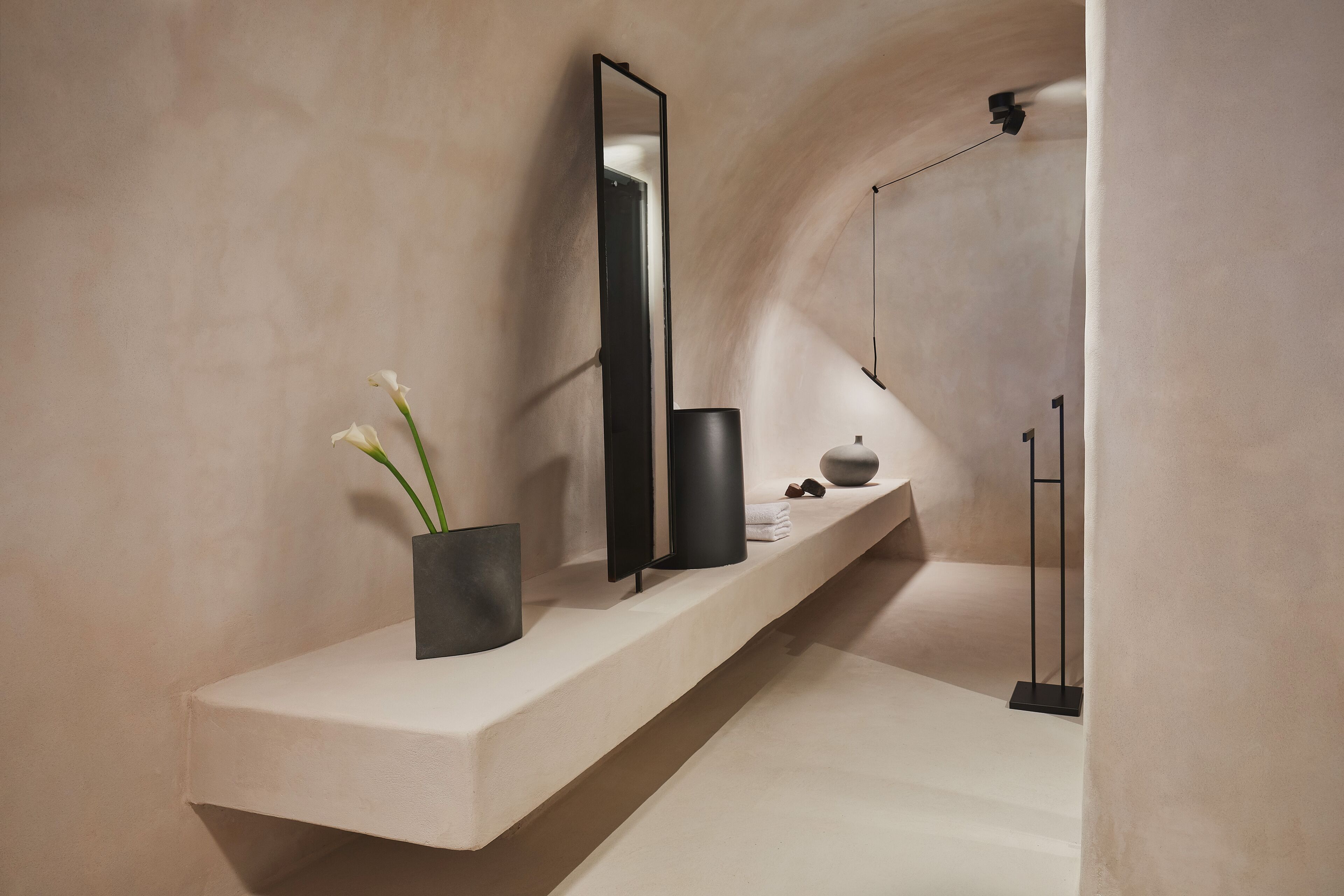 Een moderne badkamer met een minimalistisch design, met een grote spiegel, een zwarte vaas met bloemen, en een strakke zwarte vloerlamp.