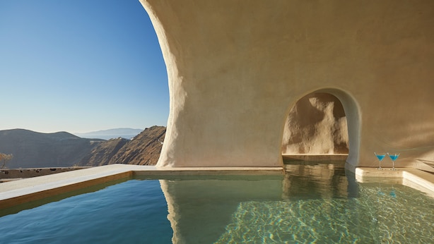 Una piscina cristalina con vista a la montaña, una pared blanca y dos copas de martini.