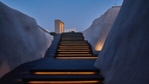 Una escalera con peldaños iluminados que ascienden, flanqueada por paredes lisas y curvas.